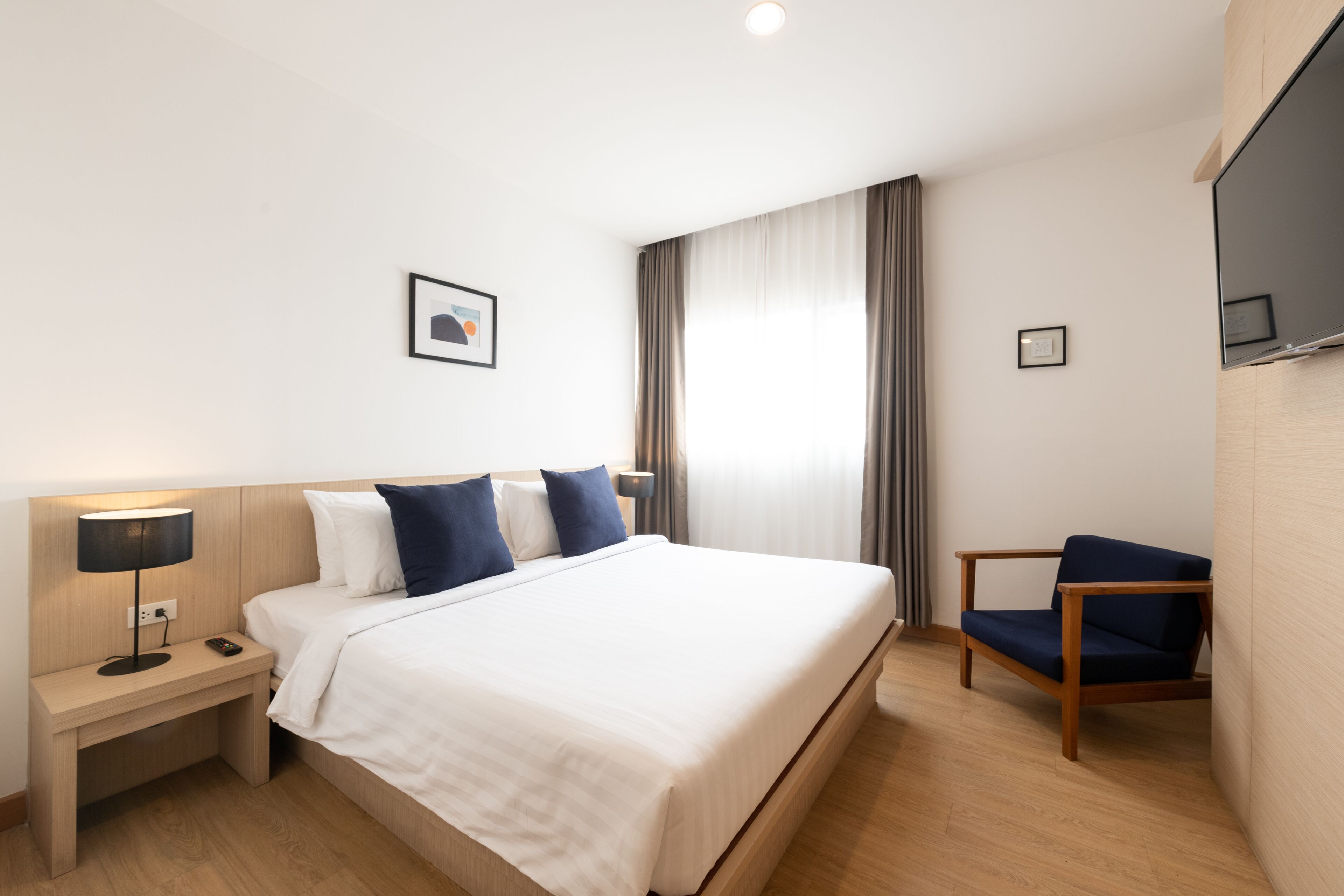 A hotel room with a bed, a nightstand, a chair, a TV, and a window with curtains.