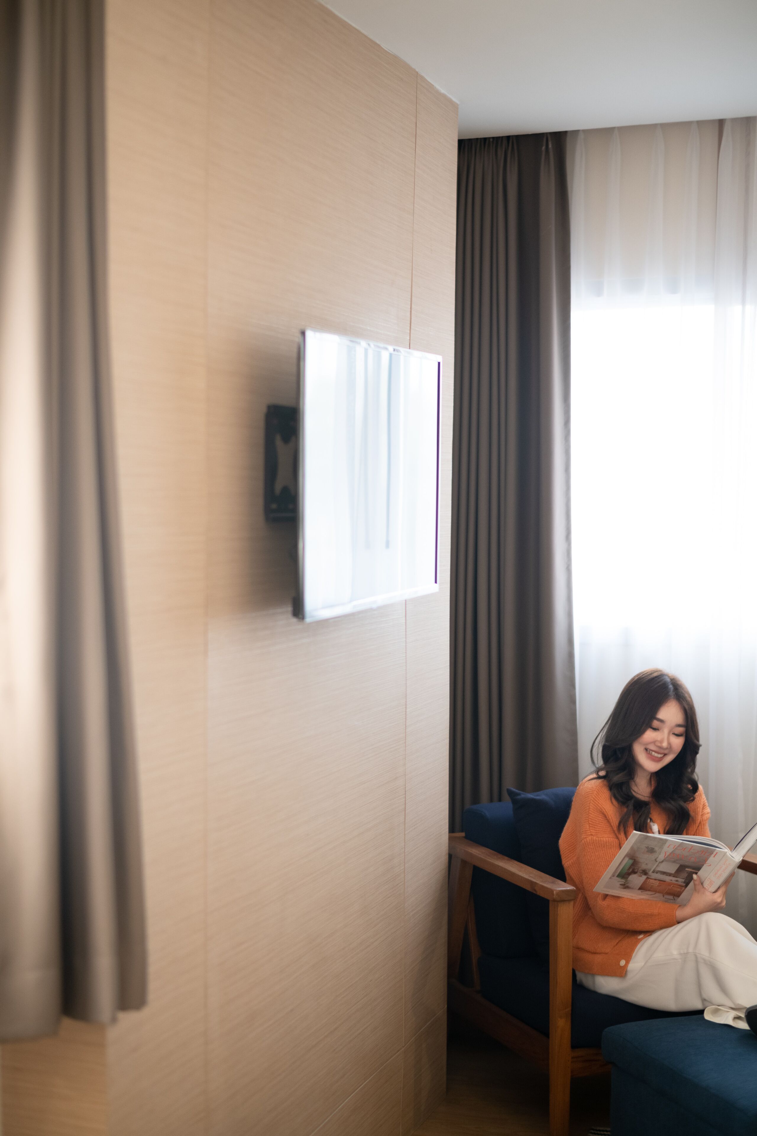 A room with a wooden panel wall, a blue sofa, and a person reading a magazine.