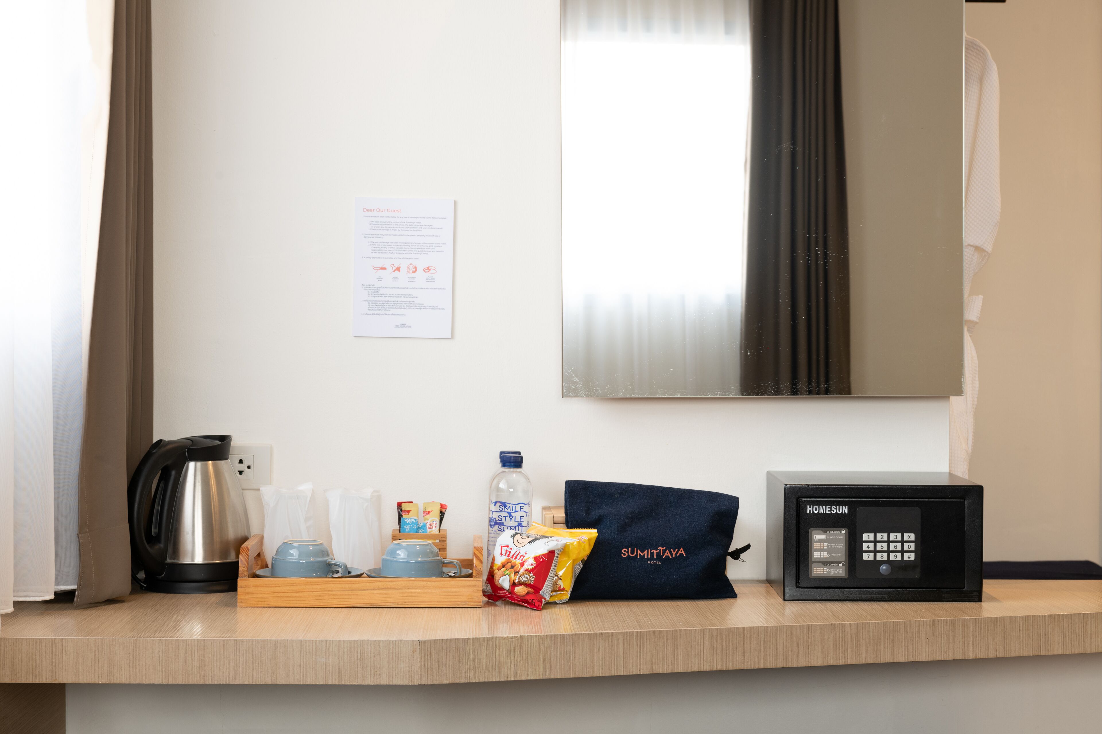 A hotel room counter with a coffee maker, a bottle of water, a bag of snacks, a microwave, and a note on the wall.