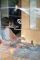 A dining table with various dishes and a glass of orange juice, visible through a window with a logo and text.