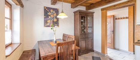 Un coin repas comprenant une table en bois, des chaises, un vase avec des fleurs, un meuble et un luminaire suspendu.