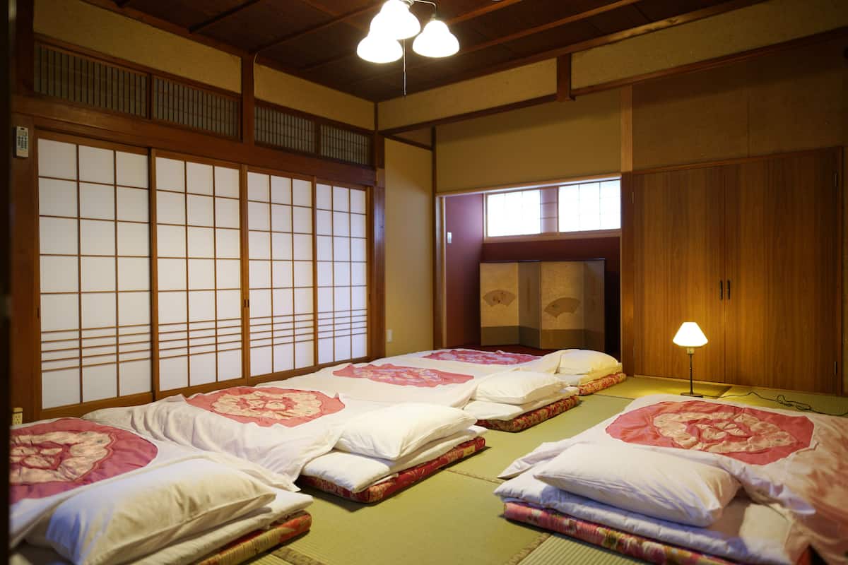 Ein traditioneller japanischer Raum mit Tatami-Bodenbelag, Shoji-Schirmen und Futonbetten mit floralen Bettdecken.