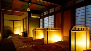 A traditional Japanese-style room with tatami flooring, shoji screens, and a low ceiling. There are three beds with wooden headboards and a futon on the floor.