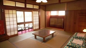 A traditional Japanese room with tatami flooring, a low wooden table, sliding shoji doors, and a futon bed.