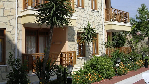 Un immeuble à plusieurs étages doté de balcons, d’une façade en pierre et d’un jardin agrémenté de fleurs et de plantes.