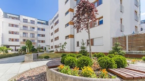Un immeuble d’appartements moderne doté de nombreux balcons, d’un jardin aménagé avec des arbustes et des fleurs, et d’un ciel dégagé.