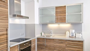 Une cuisine moderne avec des meubles de rangement en bois, un four encastré, une hotte de cuisson en acier inoxydable et un plan de travail sur lequel se trouvent une machine à café et un grille-pain.