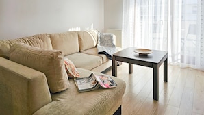 Un salon avec un canapé beige, une petite table sur laquelle se trouve un bol, et un magazine posé sur le canapé.