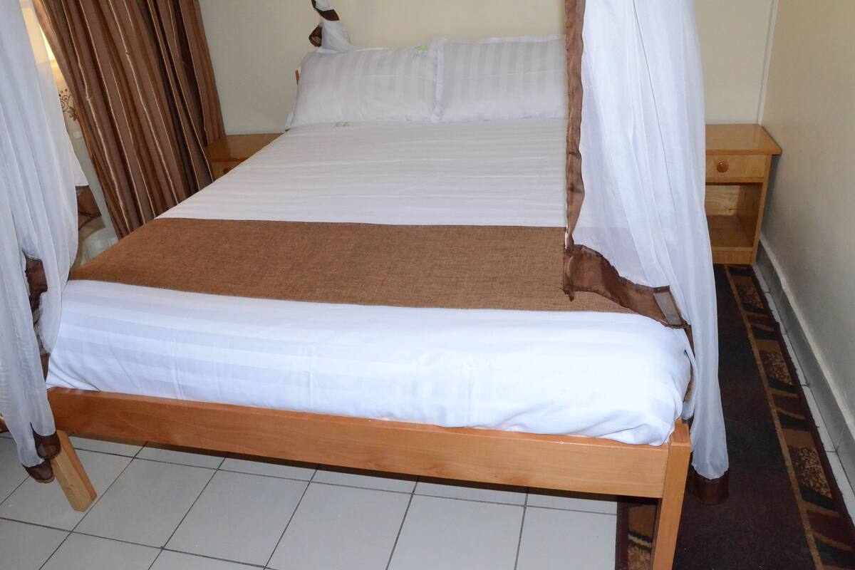 A bed with white linens, a brown blanket, and a wooden frame.