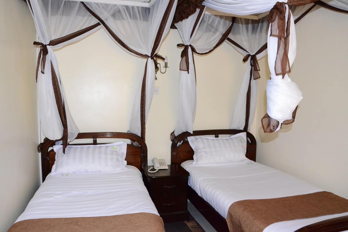 A room with two single beds, each with a wooden headboard, white bedding, and a hanging white bag.