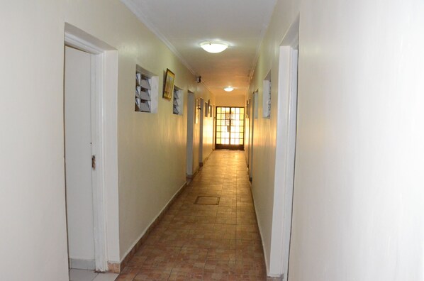A narrow hallway with white walls and a tiled floor, leading to a door at the end. - Tents Hotel (Nairobi)
