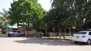 A parking area with two cars, a gated entrance, and a building with a green roof. - Tents Hotel (Nairobi)