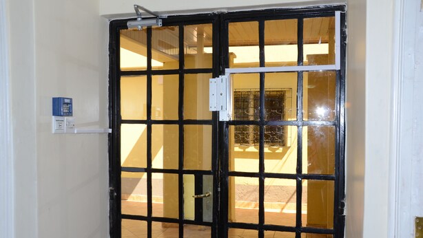 A black metal gate with a latch, a white wall, and a tiled floor. - Tents Hotel (Nairobi)