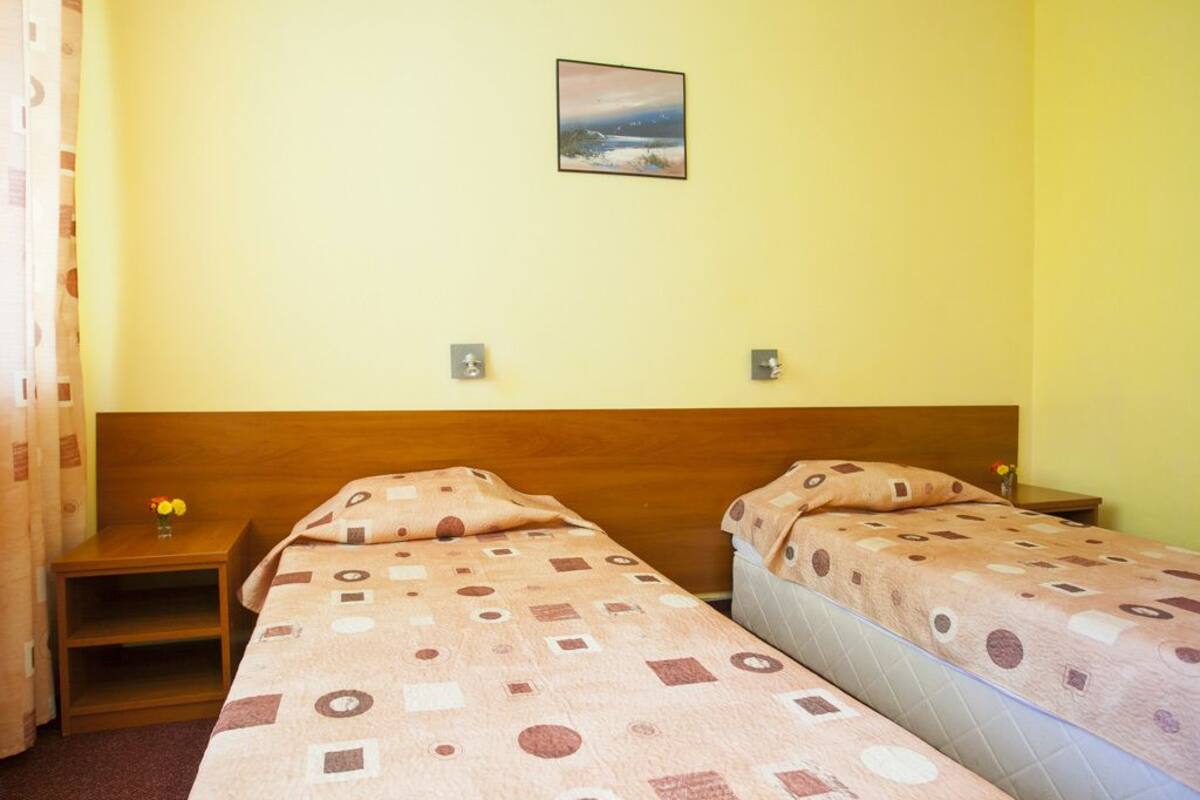 A hotel room with two beds, a wooden headboard, a nightstand with a vase of flowers, and a painting on the wall.