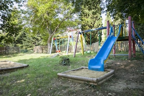A playground with a blue slide, swings, and a wooden fence.