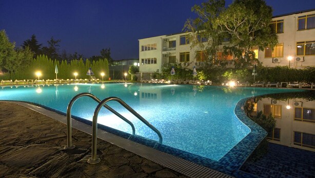 A swimming pool at night with a stone deck, surrounded by trees and a building with multiple windows and balconies. - Strandzha Hotel (Varna)