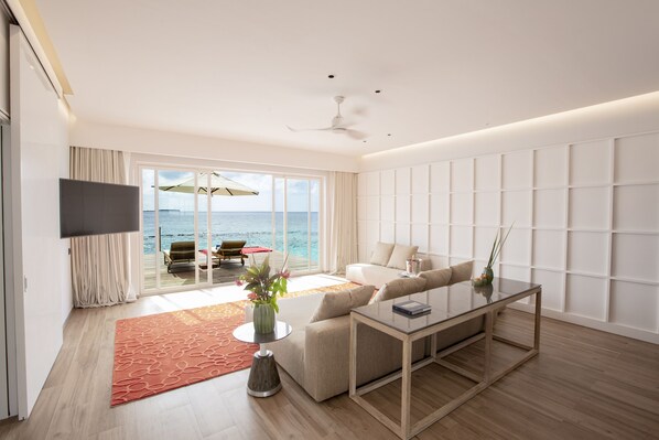 A modern living room with a large window, a flat-screen TV, a sofa, a coffee table, and a view of the ocean.