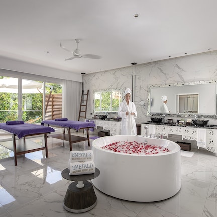 A spa room with a large bathtub filled with rose petals, a massage table, and a sign indicating the location as 'Emerald Maldives Resort & Spa'.
