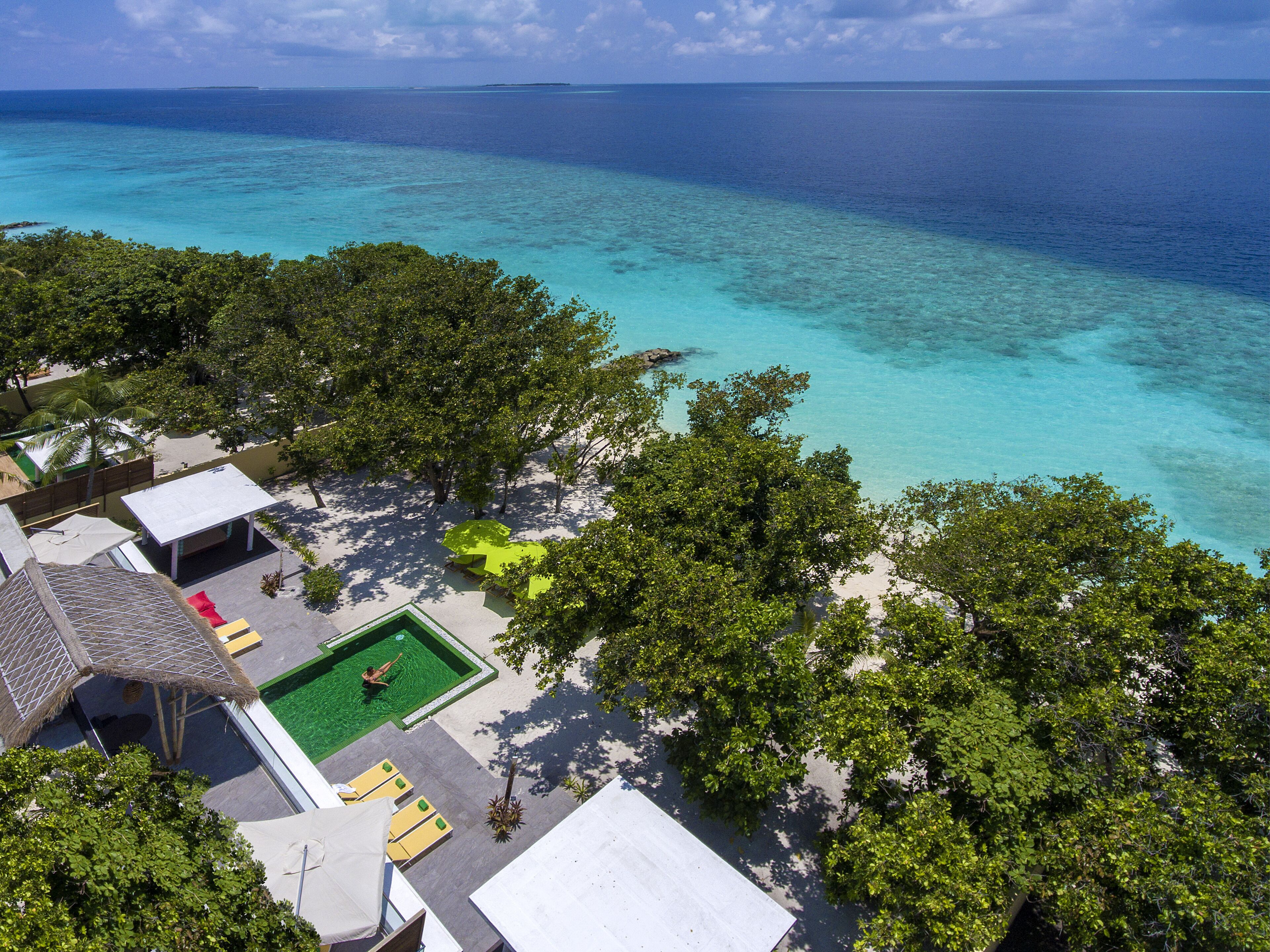 Eine Vogelperspektive zeigt einen luxuriösen Urlaubsort mit einem Swimmingpool, umgeben von üppiger Vegetation und freiem Blick auf den Ozean.