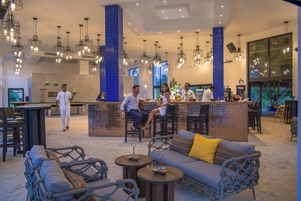 A spacious lounge area with a bar, seating arrangements, and hanging light fixtures.