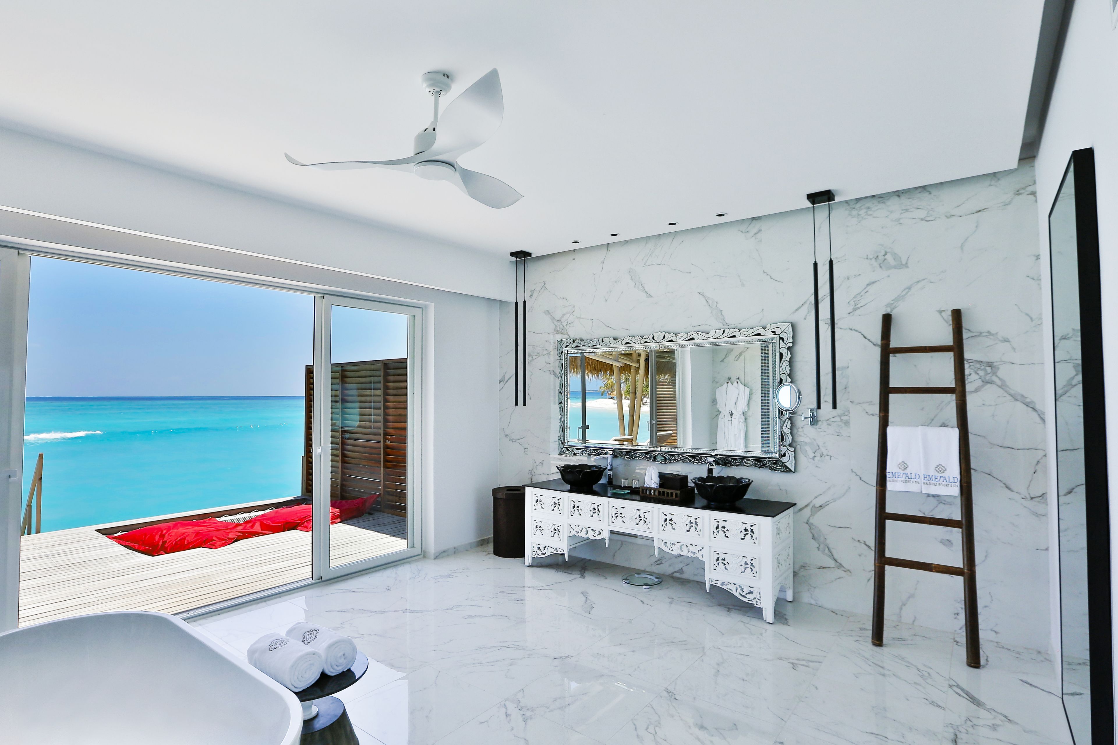 A modern bathroom with a large mirror, white marble flooring, and a view of the ocean.