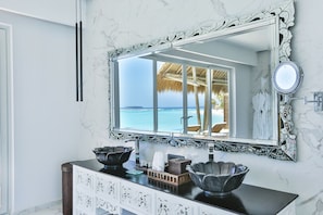 A bathroom with a marble wall, a large mirror, and a view of a beach through the window.