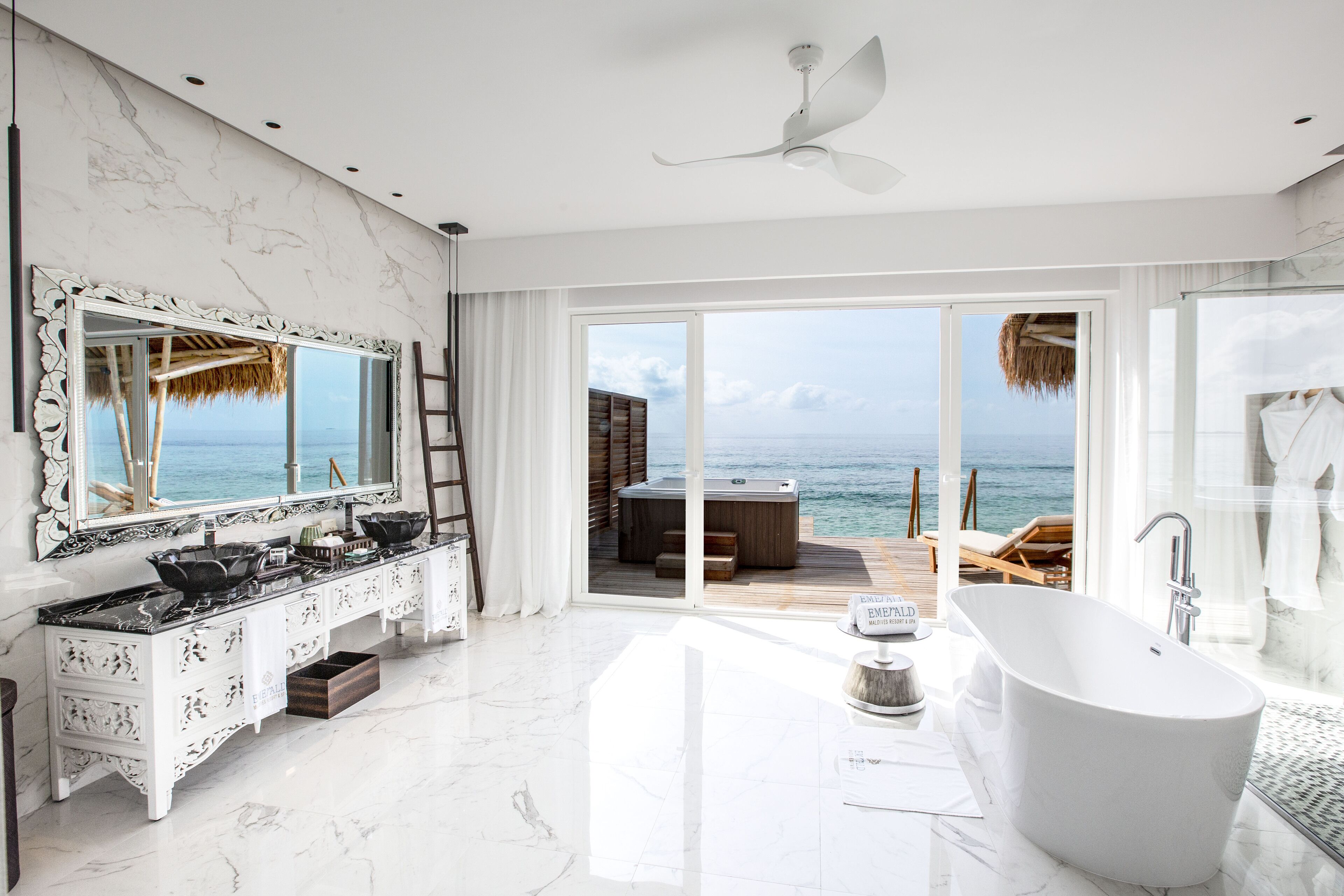 A modern bathroom with a large bathtub, a vanity with a mirror, and a view of the ocean through large sliding doors.
