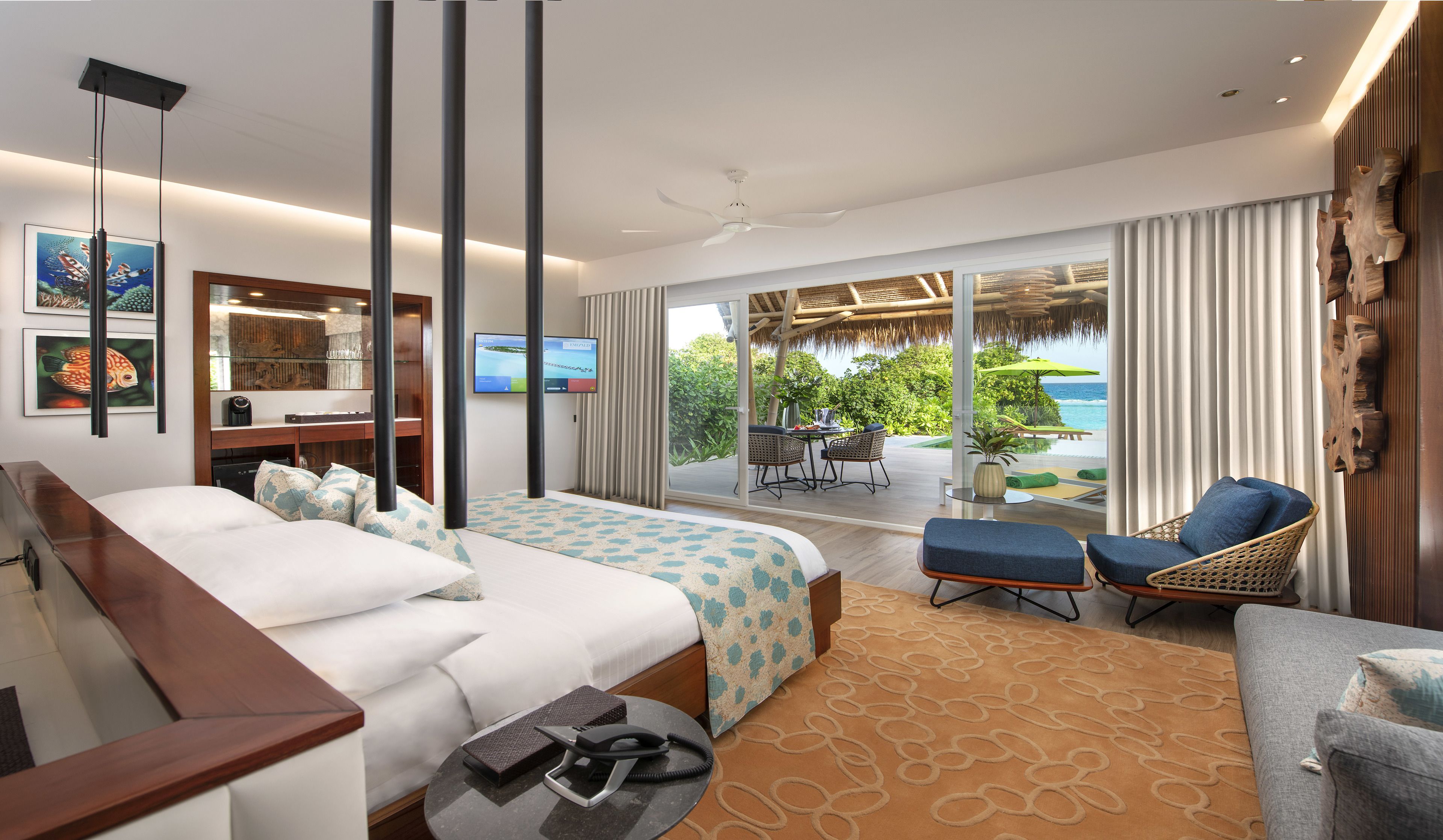 A hotel room with a bed, a desk, a TV, a balcony with a view of the ocean, and a chair.