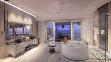 A modern bathroom with a large bathtub, a vanity with a mirror, and a view of the sea through the glass door.