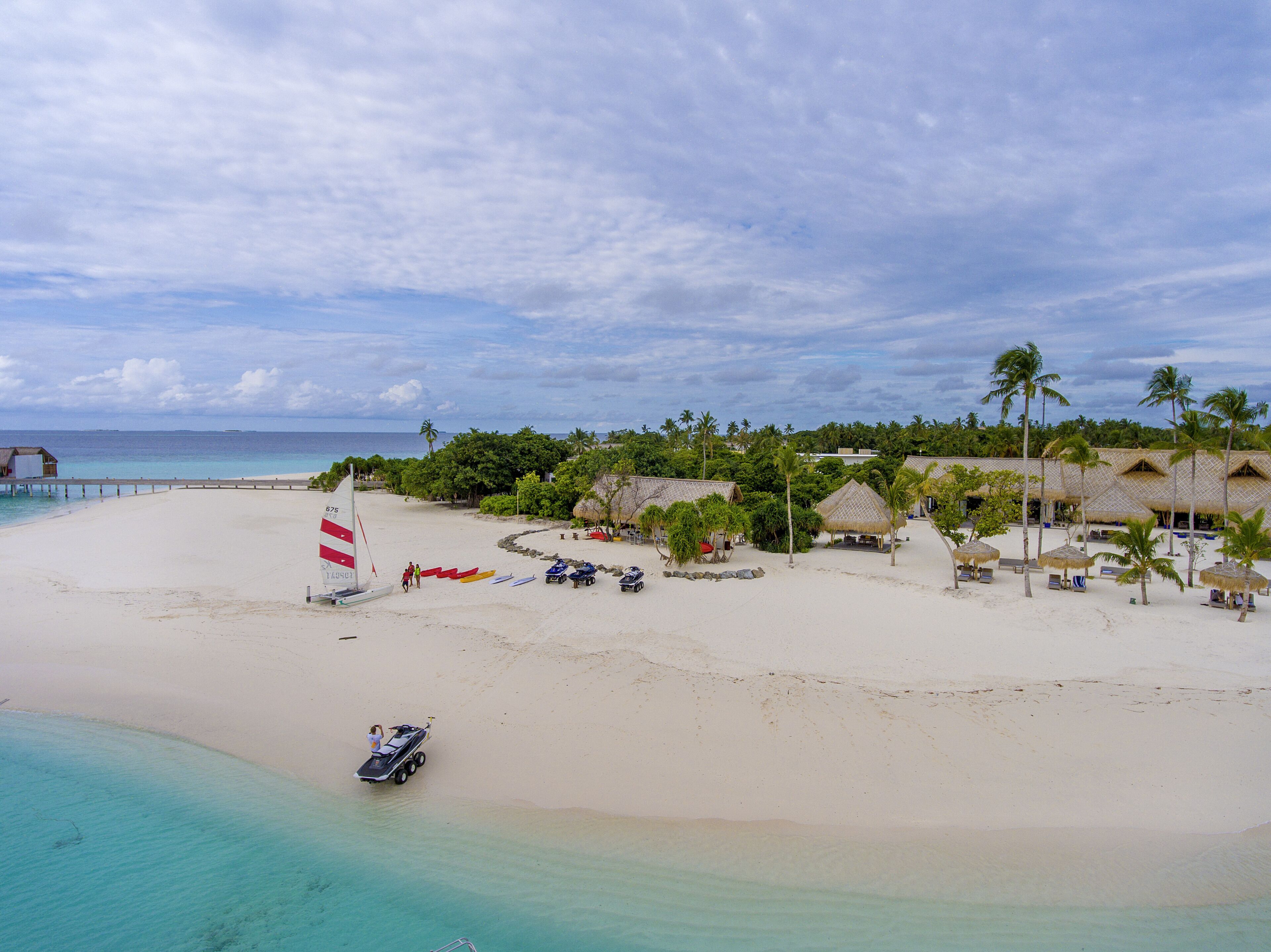 A beach with a pier, thatched-roof huts, and clear turquoise waters.