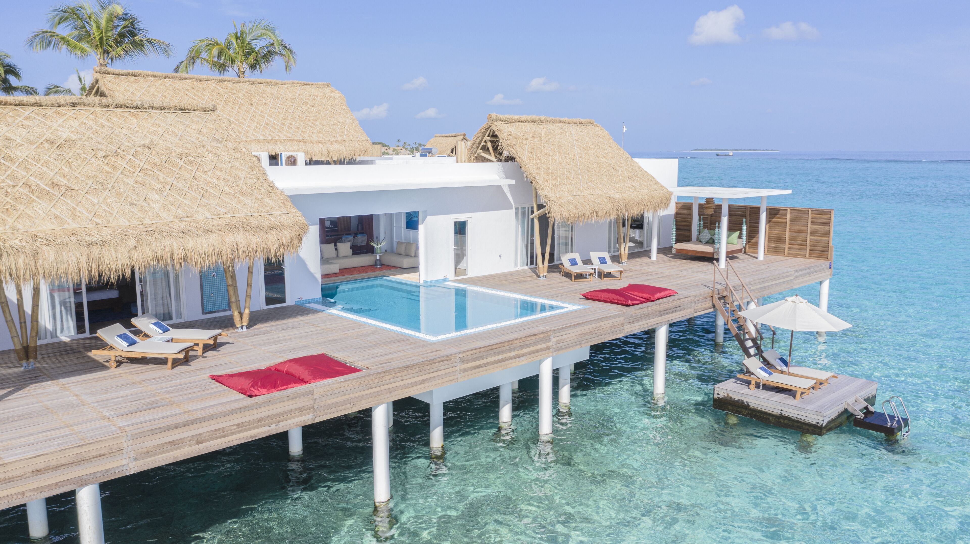 An overwater bungalows with thatched roofs, a swimming pool, and lounge chairs.