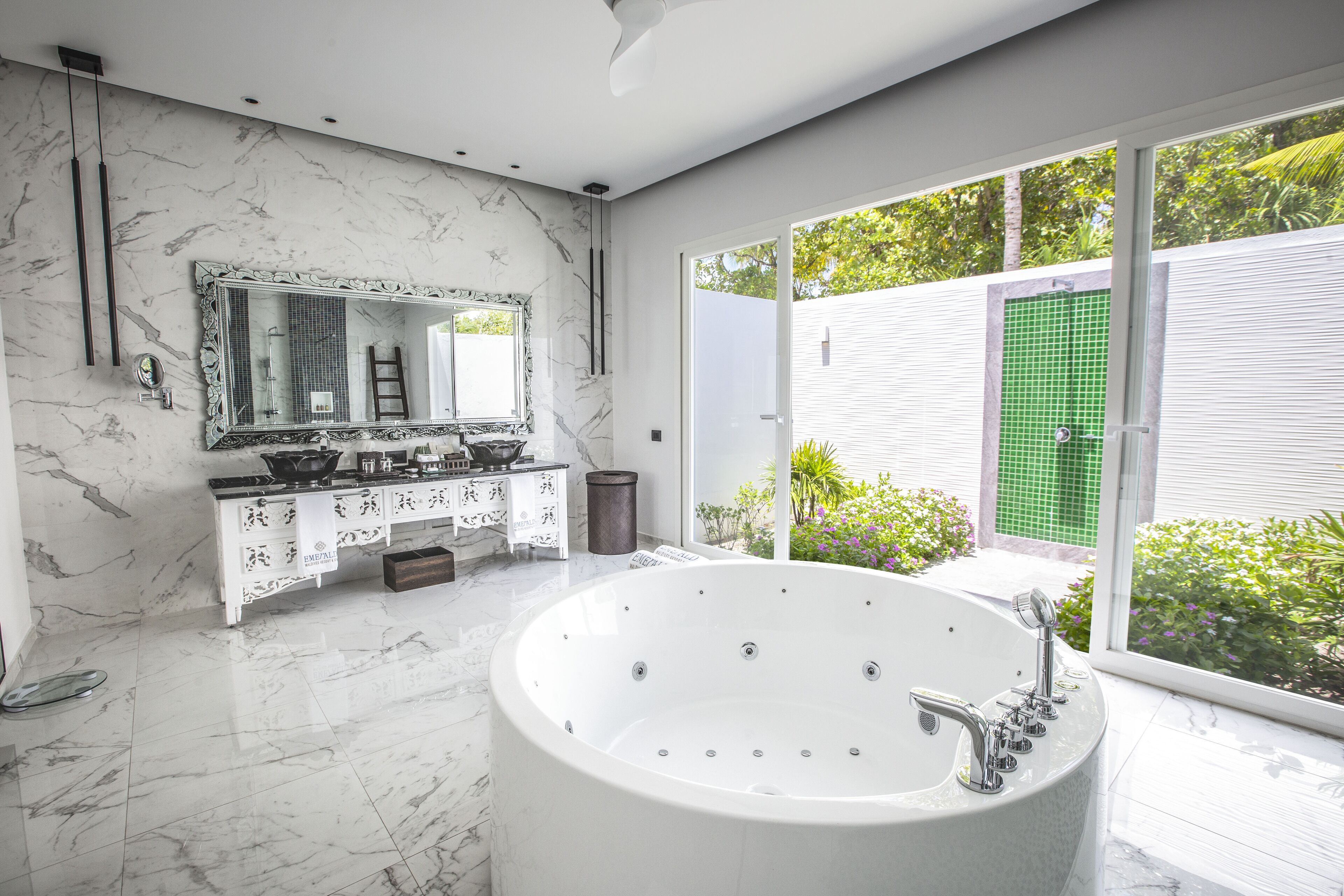 A modern bathroom with a large bathtub, a vanity with a mirror, and a view of greenery outside.