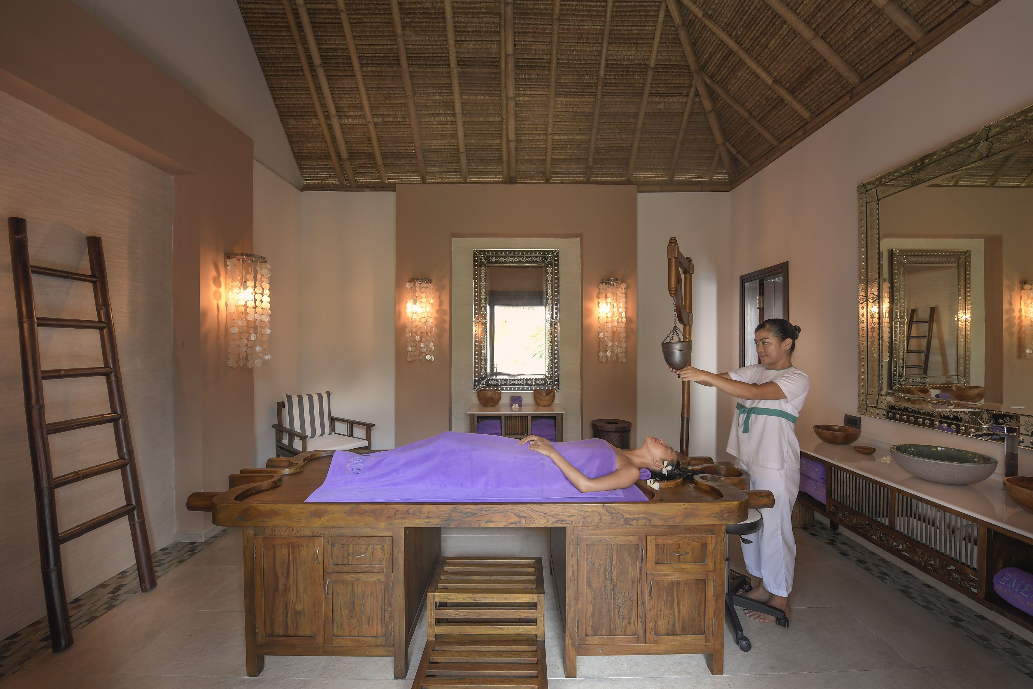 A massage room with a wooden massage table, a large mirror, and a wooden cabinet.