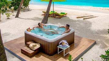 Un bain à remous sur une terrasse en bois, avec vue sur la plage et l’océan.