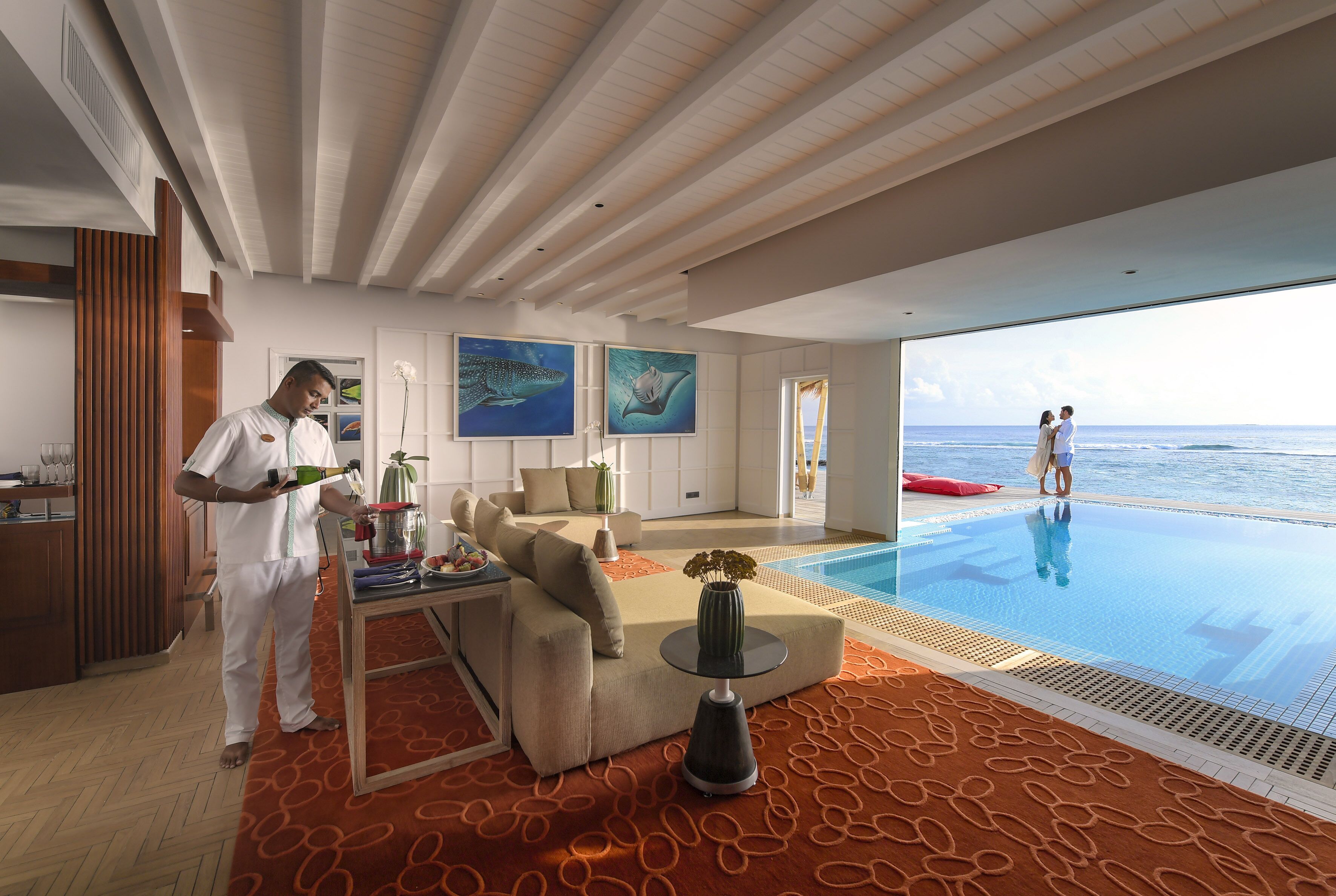 A modern hotel room with a large window overlooking a pool and the sea.