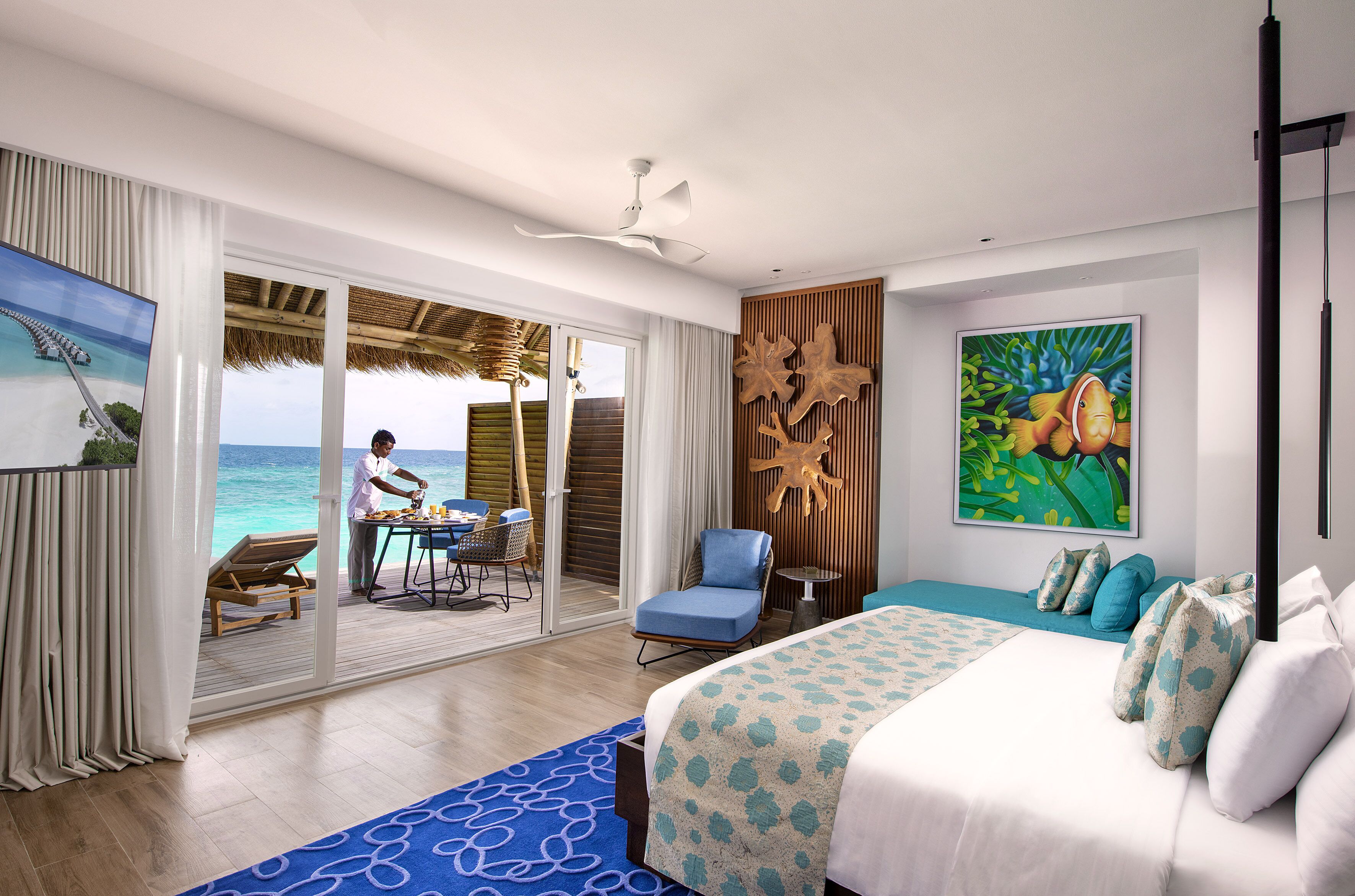 A hotel room with a bed, a chair, a table, and a view of the ocean.