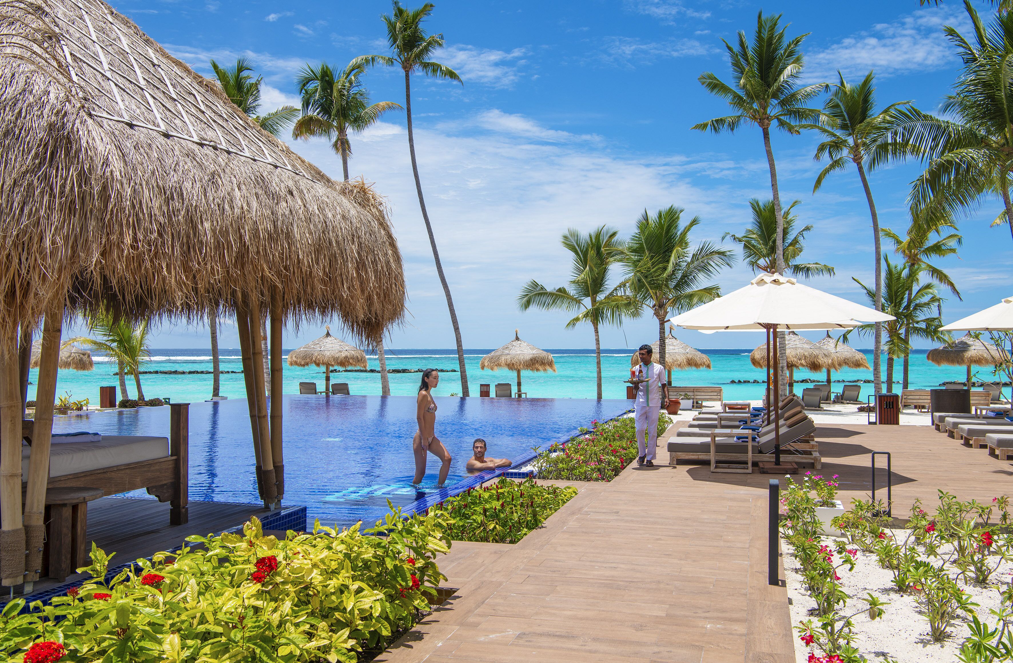 A resort pool area with thatched umbrellas, lounge chairs, and a wooden deck.