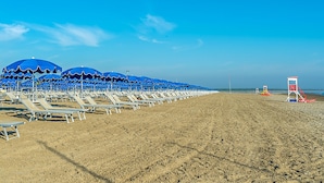 A beach with rows of blue umbrellas and white lounge chairs. - 3 bedroom cozy home in Albarella RO (Albarella RO)