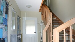 Una escalera de madera que sube a un piso superior, una puerta blanca con un panel de vidrio esmerilado y un mueble de almacenamiento gris con cajones.