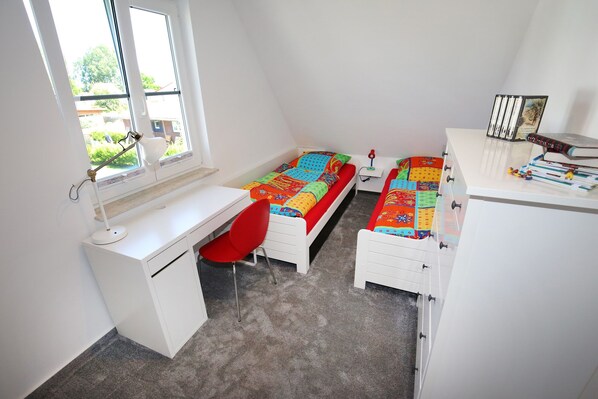A bedroom with two single beds, a desk, a chair, and a small bedside table.