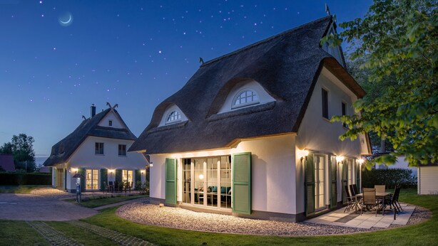 Una casa con techo de paja, contraventanas verdes y un patio bien iluminado.