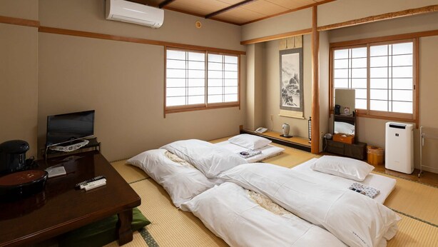 A traditional Japanese-style room with tatami flooring, two single beds, a desk with a television, and an air conditioning unit. - KATSUYA Inn (Wakayama)