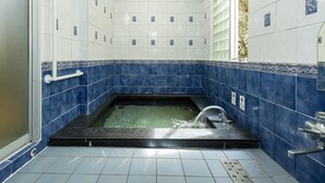 A bathroom with a bathtub, blue and white tiles, a handrail, and a window with a view. - KATSUYA Inn (Wakayama)