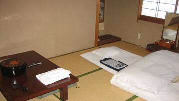 A traditional Japanese room with tatami flooring, a low wooden table with a black container and a remote control, and a bed with white bedding.