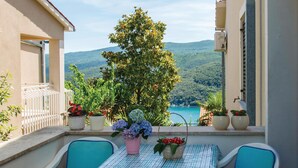 Un balcón con mesa y sillas, plantas en macetas y vistas a un lago y montañas.