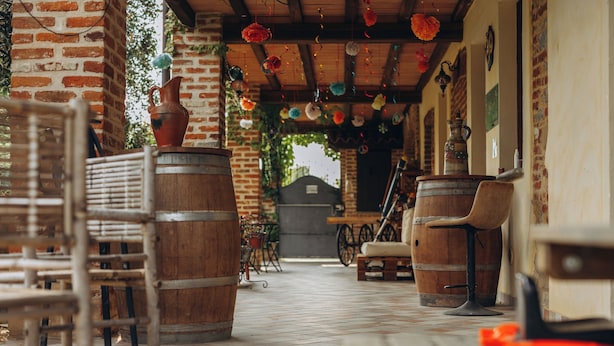 Un espacio al aire libre rústico con mobiliario de madera y barriles, decorado con adornos colgantes.
