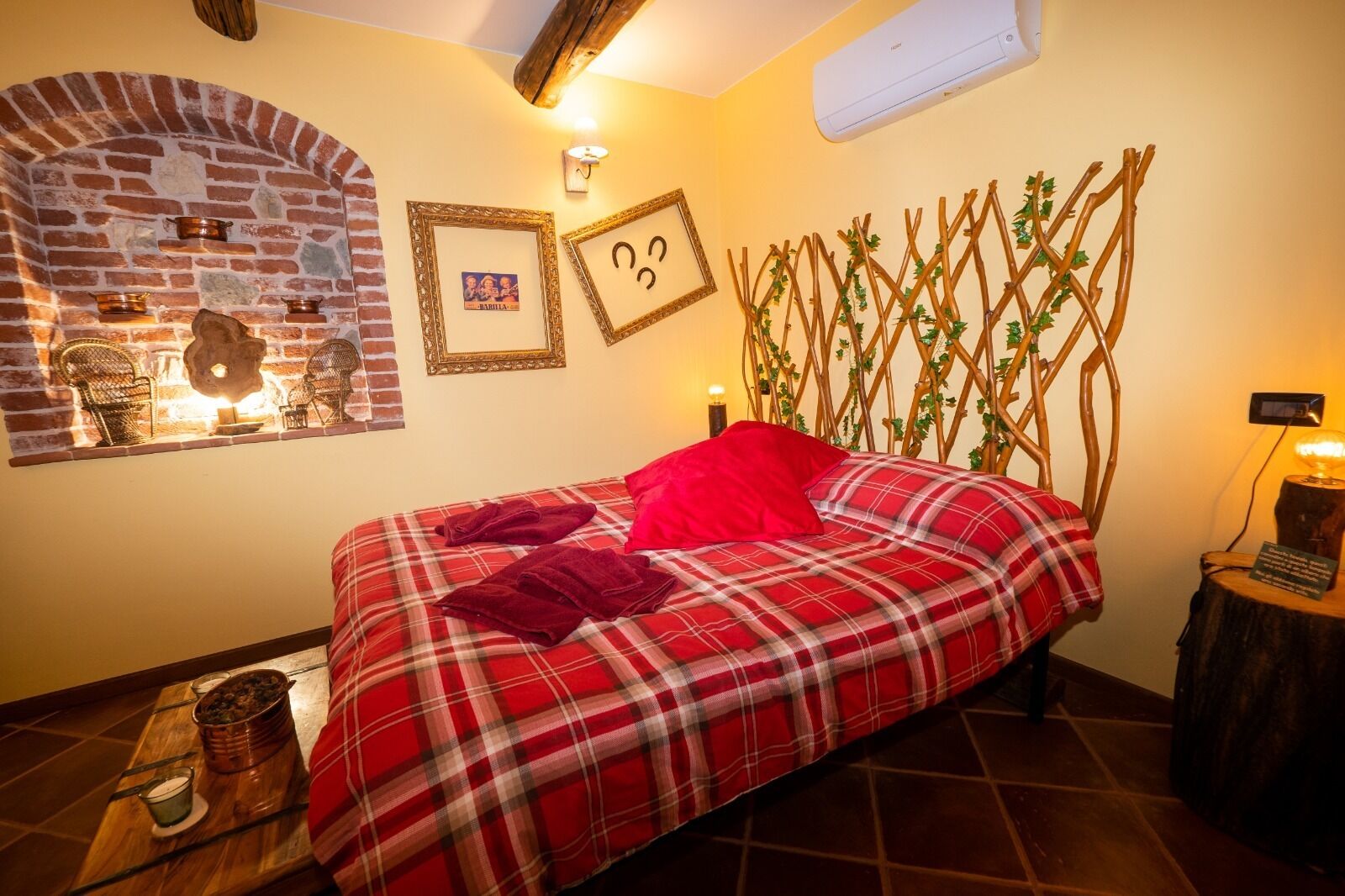 Una habitación acogedora con chimenea de ladrillo, una cama con colcha escocesa y un enrejado de madera con follaje.