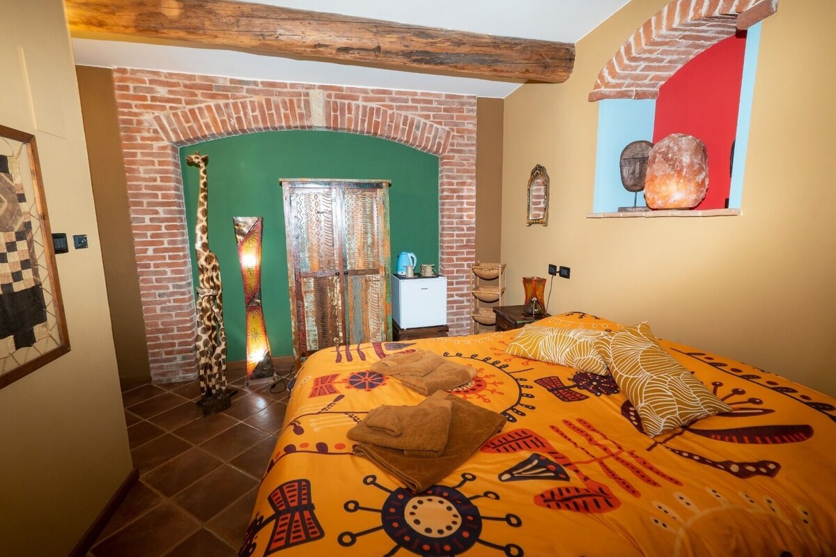 Una habitación con cama, pared de ladrillo, arco verde y ventana decorada con piedras.