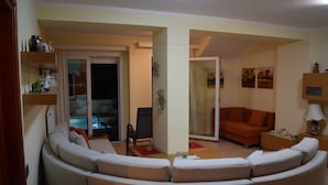 Una sala de estar con un sofá curvo, una mesita y una silla. Hay una puerta corrediza de vidrio que da a un balcón.