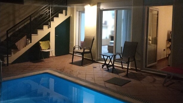 Una piscina con una escalera que lleva a un área cubierta con sillas y una mesa.